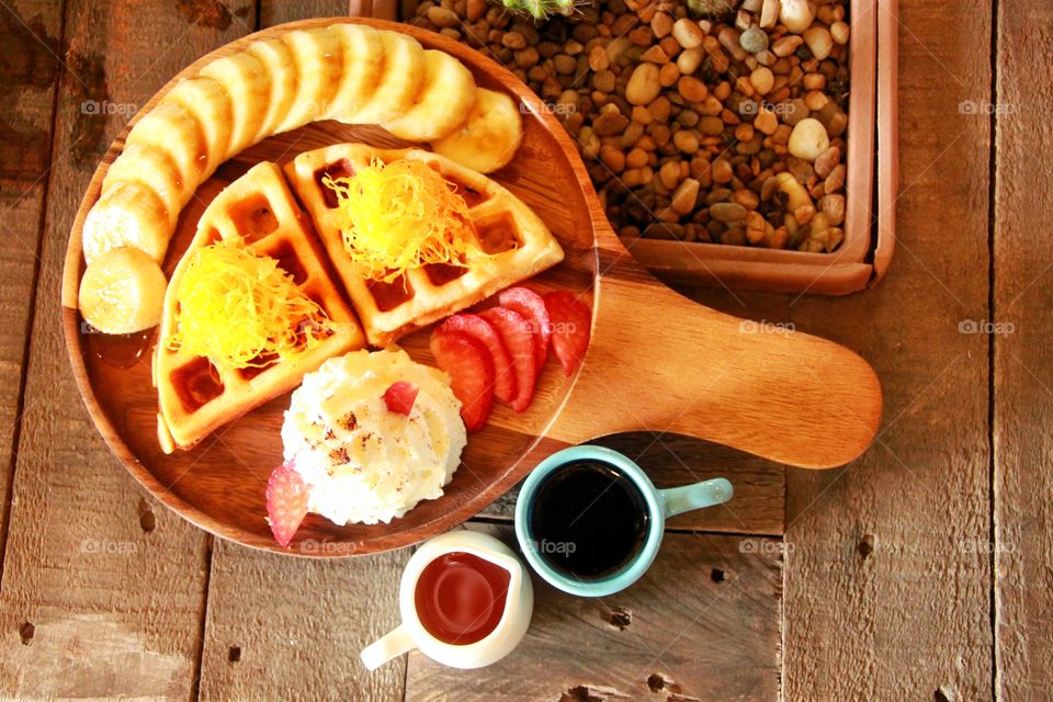 The waffle bread is sprinkled with Thai desserts, along with sliced ​​bananas, placed on the side of the curved tray and has whipped cream for added flavor.  And chocolate and strawberry juice are added for adding to the dessert for an extra level.