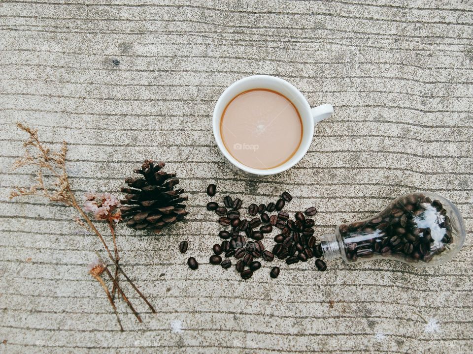 A White cup of coffee and coffee beans in glass bottle on concrete floor