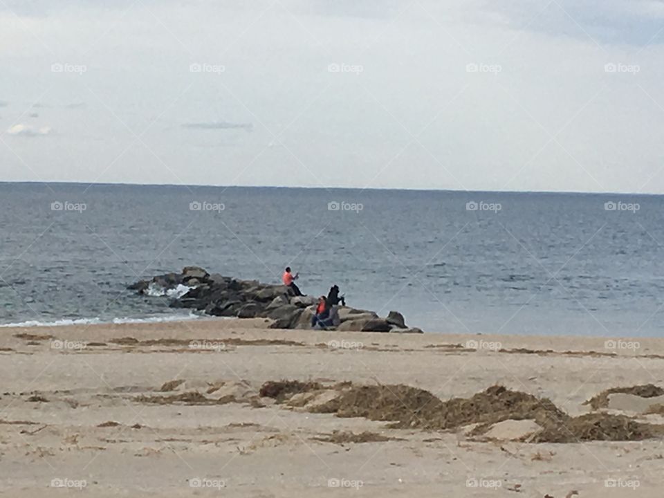 Two men fishing on rocky pier on the beach. 