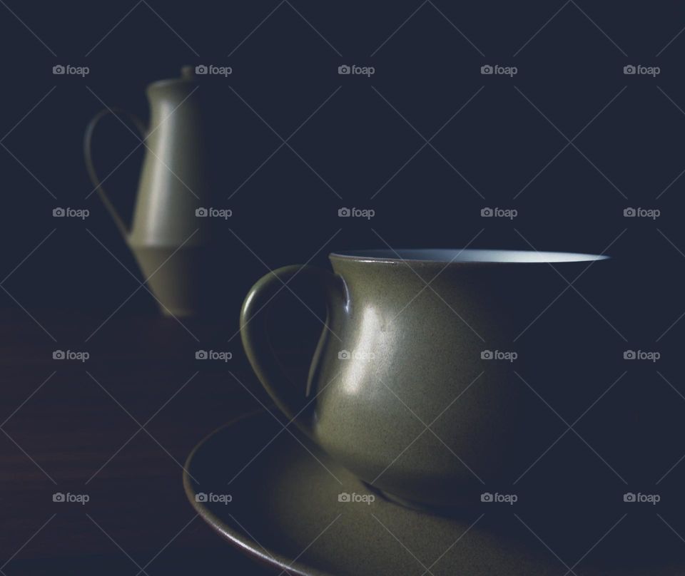 Coffee pot with cup and saucer under split lighting 