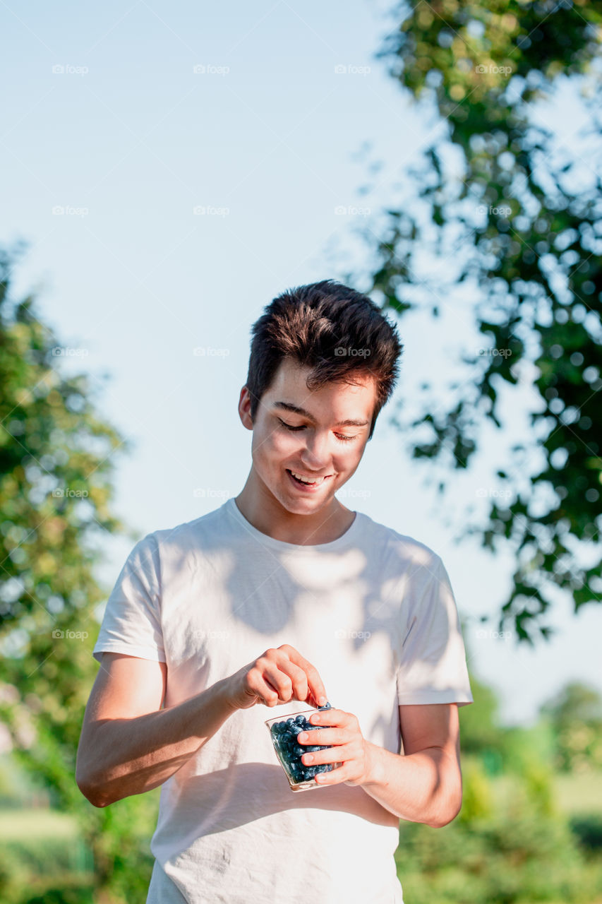 Boy enjoying the fresh blueberries outdoors standing in a garden in the summer. Young boy wearing white t-shirt