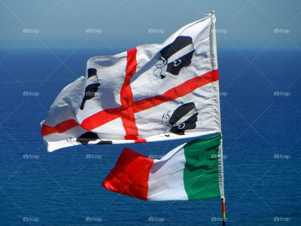 Sardinian and Italian flags in front of mediterranean sea