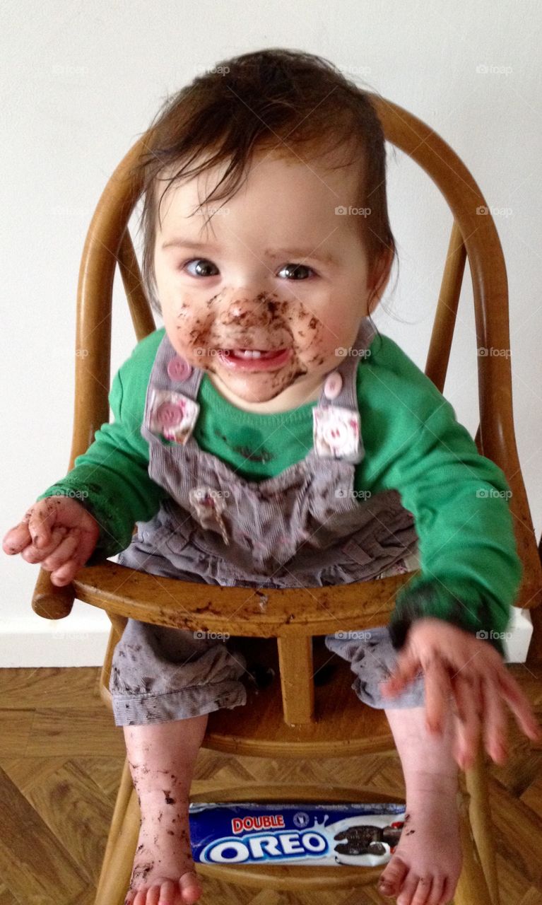 Baby sitting in high chair face covered in chocolate. Baby loves biscuits laughing