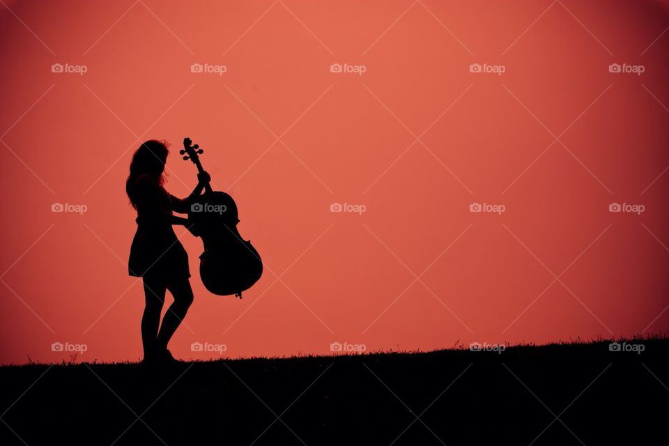 Girl with a cello against a red sky.