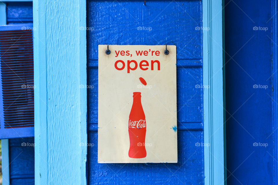 Vintage Coca-Cola open sign hanging on a bright blue building