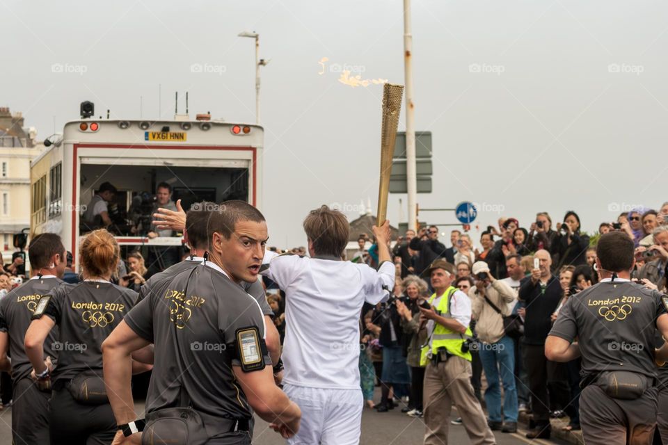 A crowd of people watch the Olympic Torch relay pass along the seafront of Hastings UK in 2012