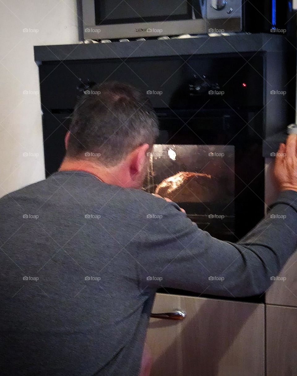 Kitchen.  Making homemade bread.  A man looks into the oven and watches how bread is baked