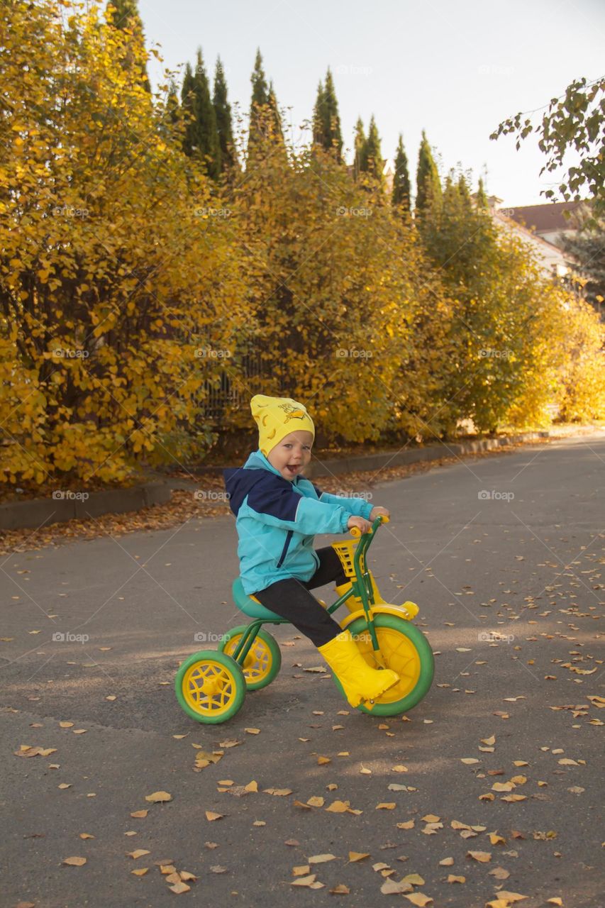A little boy in yellow boots is learning to ride a bike in the park.
