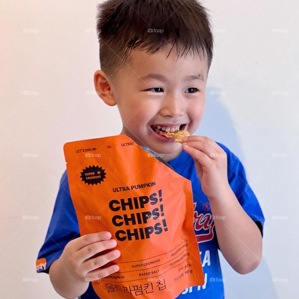 Asian boy eating Halloween trick or treat snacks made of pumpkin chips