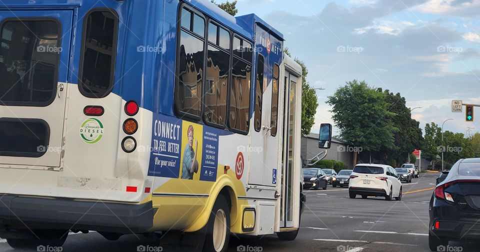 yellow white and blue public bus transporting passengers through commuter traffic in Oregon