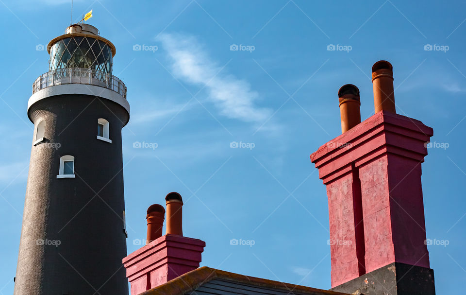 2 red chimney stacks, next to a lighthouse, against a blue sky