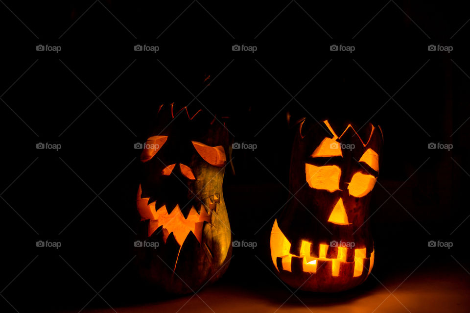 Two evil pumpkins for Halloween. An evil face is carved on the pumpkin, a candle is burning inside, in a dark room.