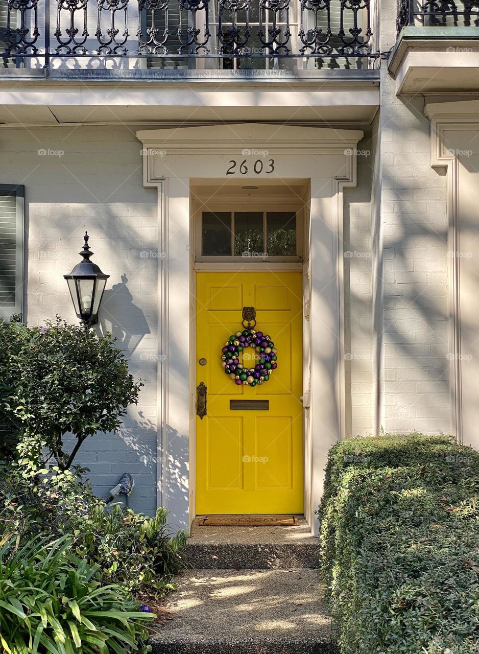 A yellow front door with a Mardi Gras wreath
