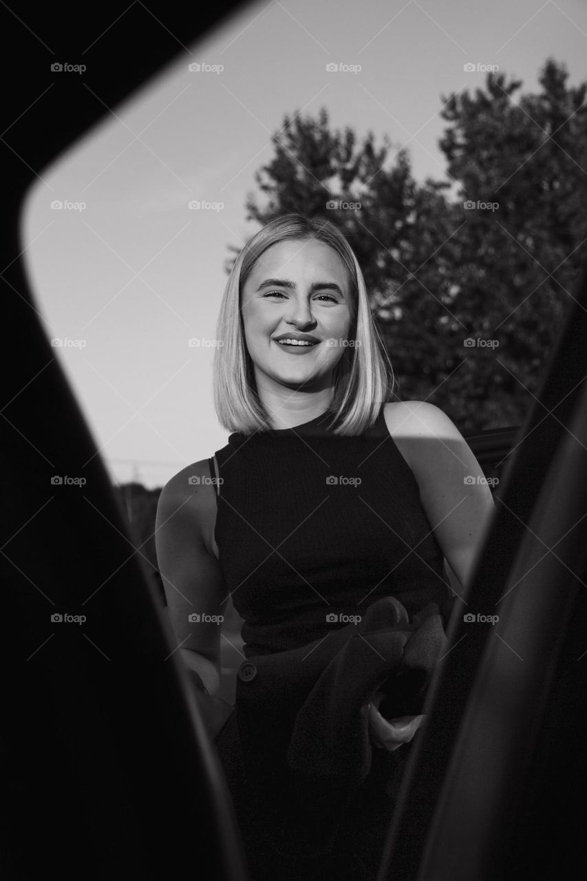 A girl smiling outside the car in black and white filter