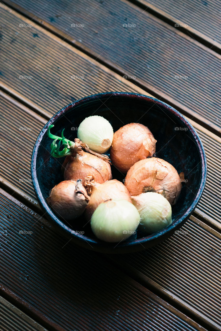 Closeup of bowl of onions sprinkled raindrops on wooden table