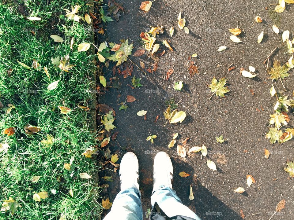 Feet on asphalt way in autumn. Man standing on asphalt way, park with autumn foliage