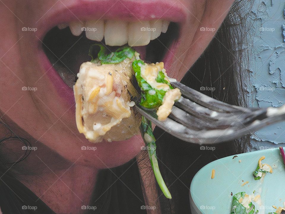 Glimmers close-up of eating a delicious salad with Colby Jack shredded cheese, spring mix lettuce and spinach with parmesan and Italian dressing and mayonnaise on a fork with bowl aside. Mouth opened smiling to eat with hair and grey blue background.