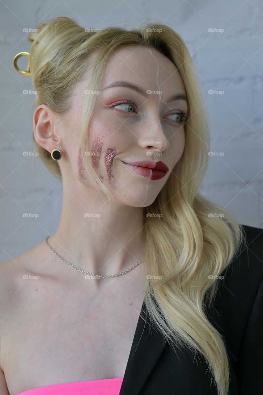 Close-up portrait of a blonde girl with different make-up on half of her face on white background