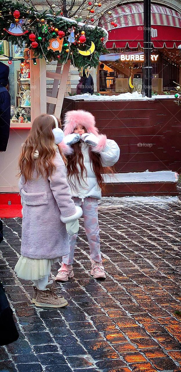 Happiness. On the winter street there are two girls who are warmly dressed. One girl smiles and shows something and tells her friend