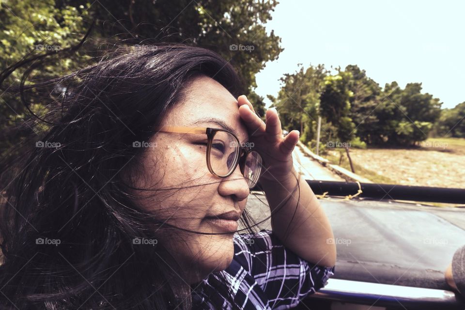 Close up side view of an asian natural woman with eyeglasses with no make up on a windy day travelling in a vehicle.
