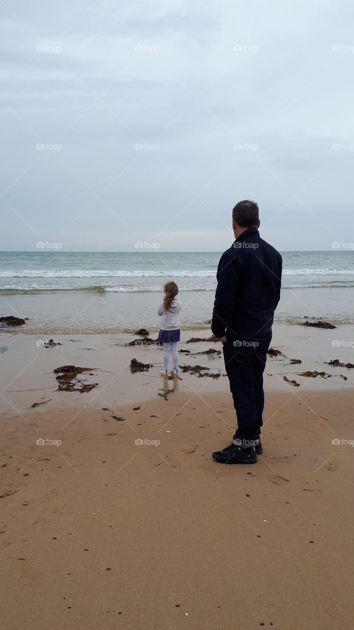 father and  daughter staring at the sea, standing by the water