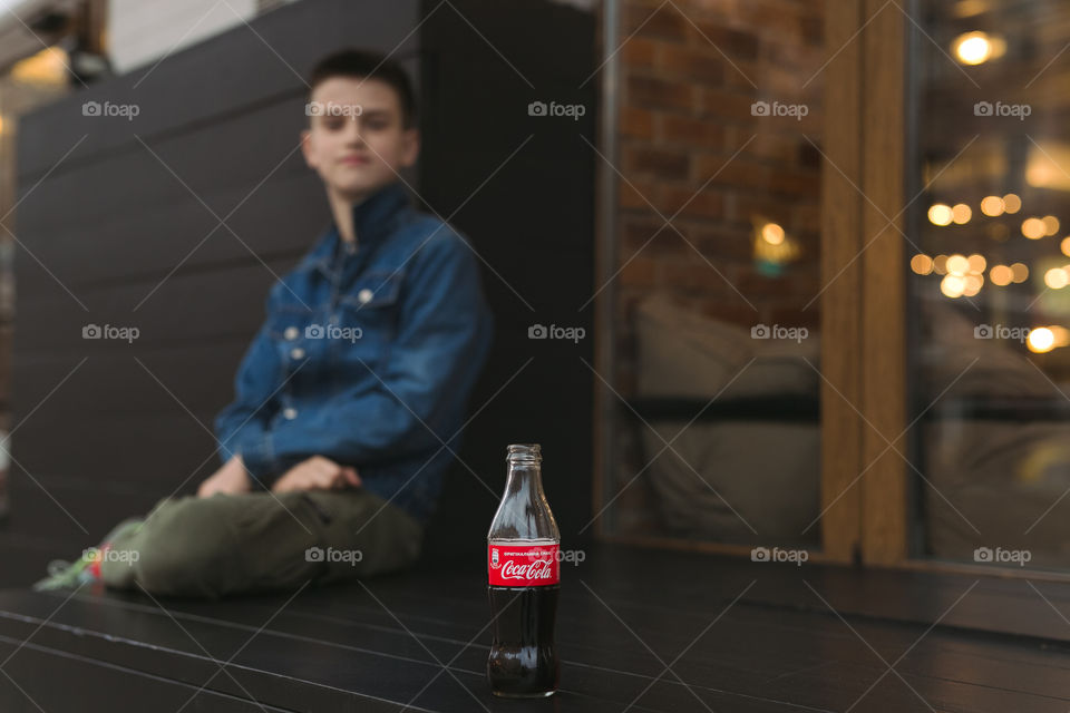 Cute guy seating at the street, drink Coca-Cola 