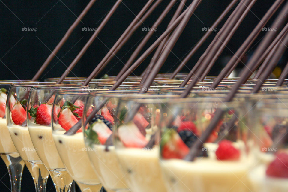 Rows of single serving desserts in elegant wine glasses topped with fresh fruit and a stick of chocolate