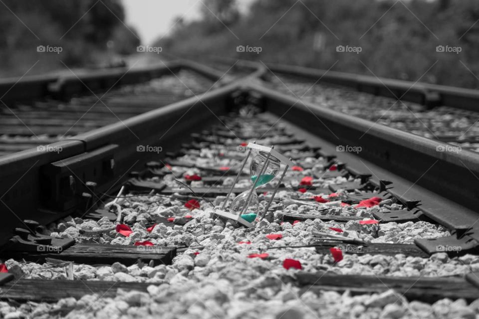 Timeless moments with red petals in black and white teal sand in hourglass