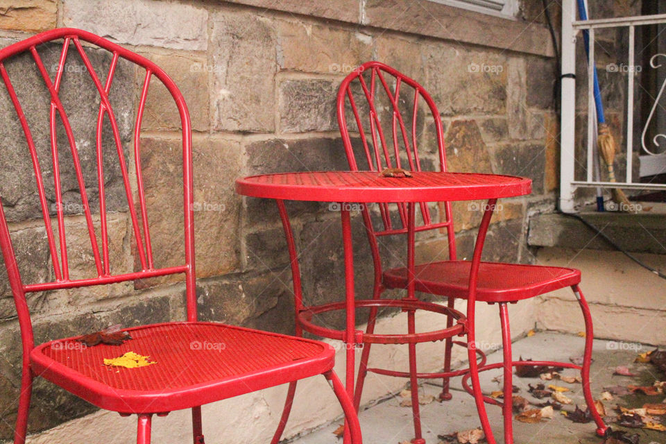 A radiant red table and chair set beautifully set against a large brown and gray Cobblestone wall.