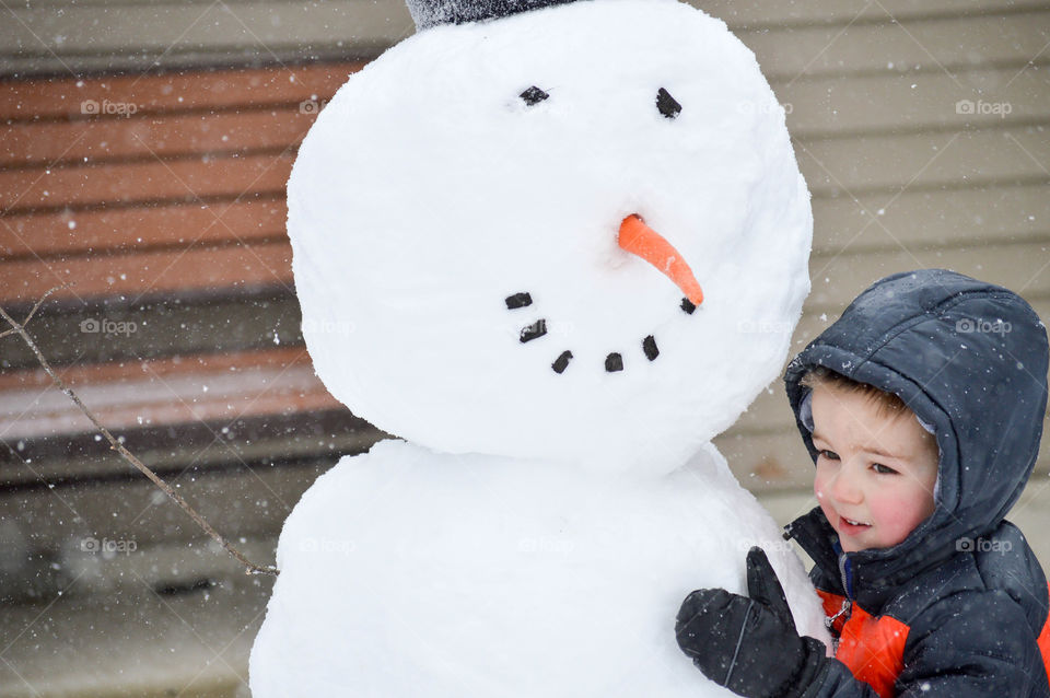 Toddler boy hugging a homemade snowman