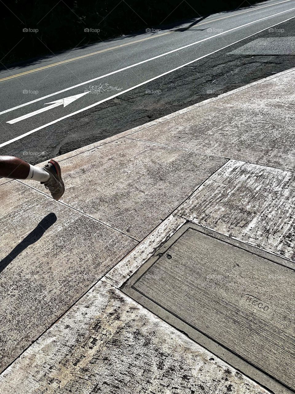 Left foot and leg of male runner going slightly downhill on sidewalk near bike path showing direction arrow 