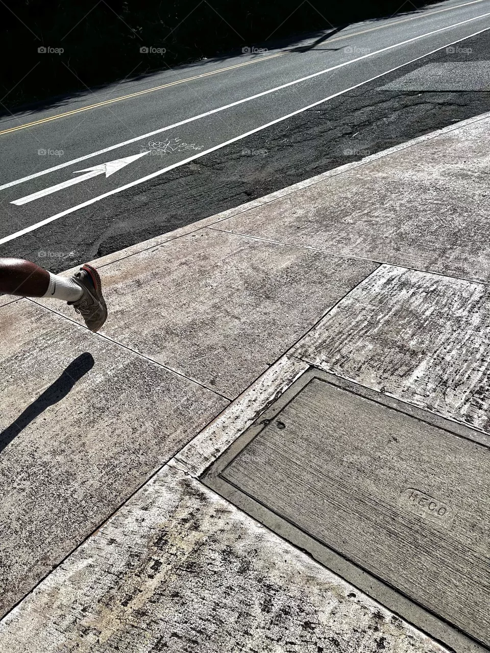 Left foot and leg of male runner going slightly downhill on sidewalk near bike path showing direction arrow 