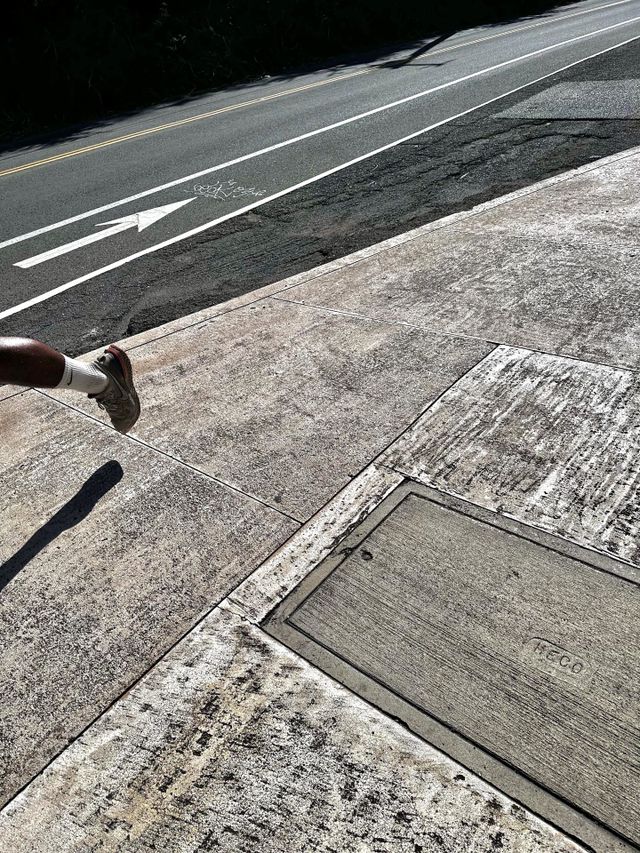 Left foot and leg of male runner going slightly downhill on sidewalk near bike path showing direction arrow 