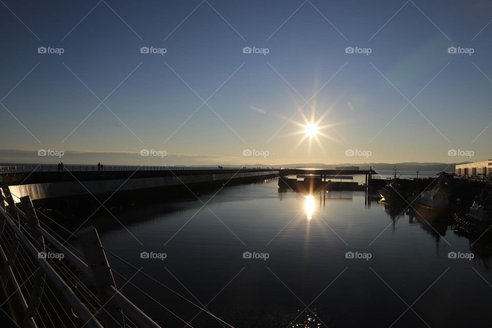 Sun reflecting in the ocean by the breakwater 