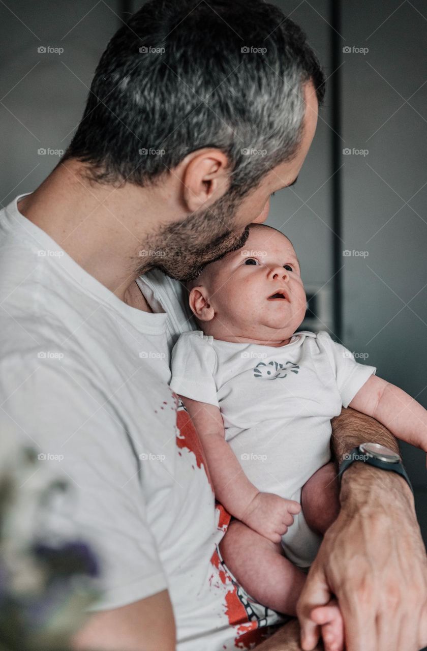 Dad holding his baby boy in hands and kissing him on forehead