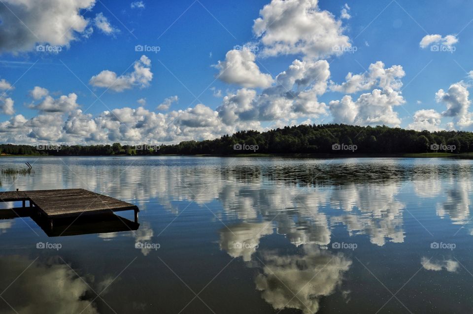 summertime at the lake in poland - wooden pier and forest under the blue cloudy sky