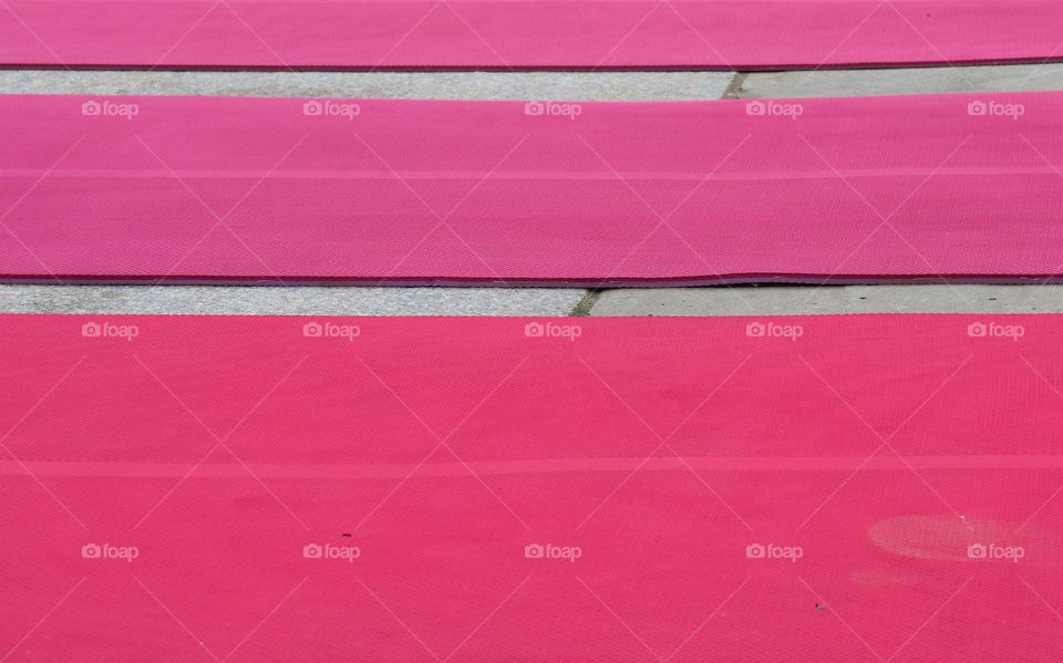 Pink yoga mats lined up on a park walkway in preparation of an outside yoga  class.