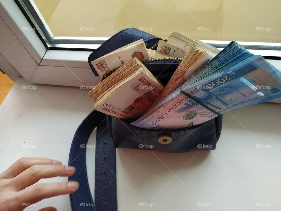 A hand reaches for a handbag in which there is a large amount of money. Almost four million rubles in a small blue handbag