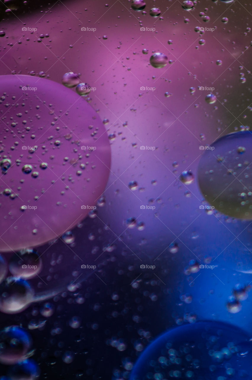 Bubbles of vegetable oil in clear water on a glass and transparent lid from a frying pan on colored paper.