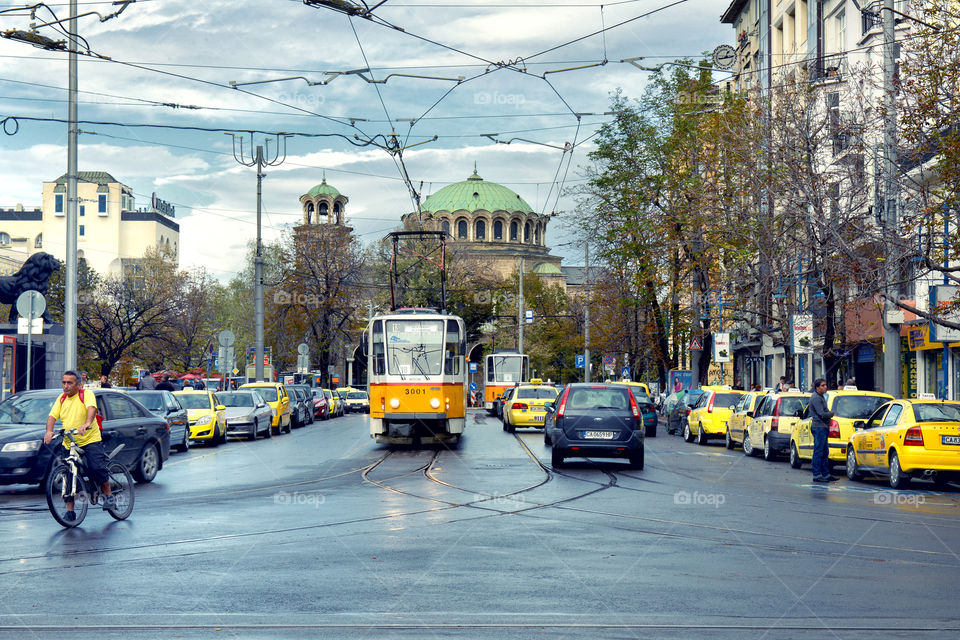 the tram is on the central street with a lot of yellow taxes