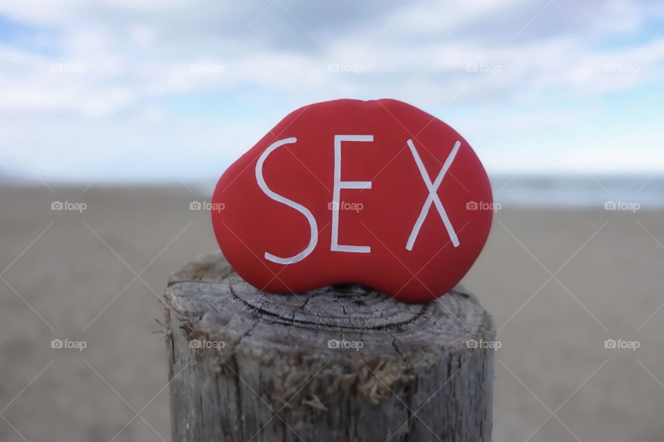 Sex text on a red colored stone on a wooden pole at the beach