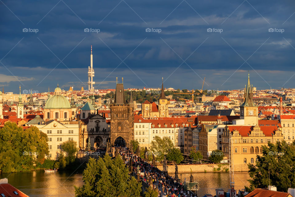 Charles Bridge and Stare Mesto in the rays of the setting sun on the background of the dark clouds. Prague, Czech Republic