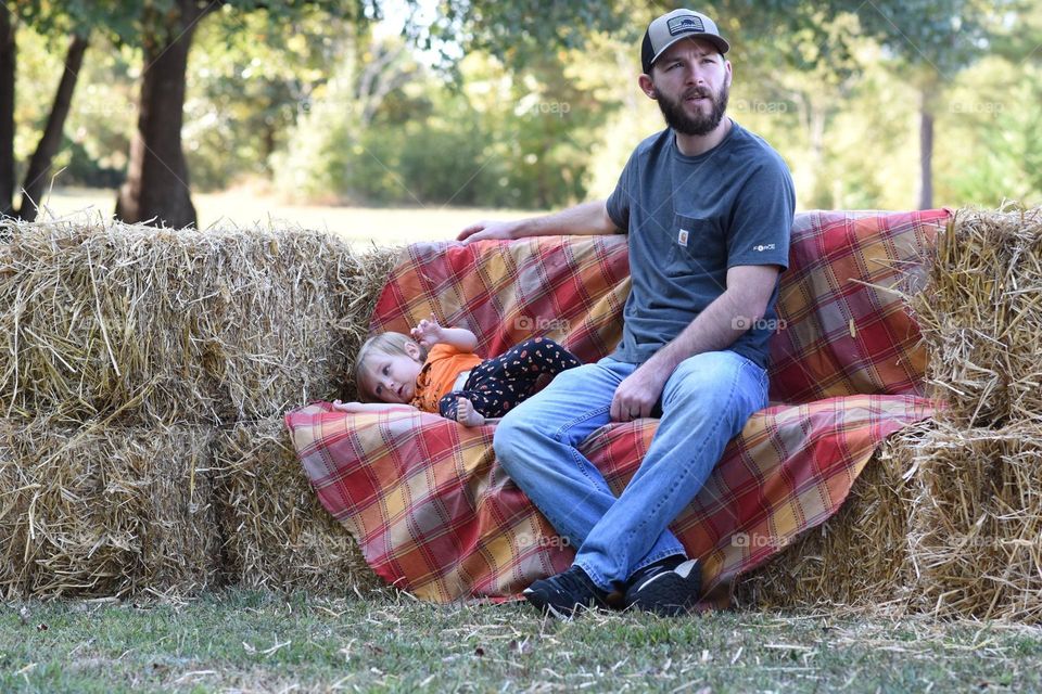 A funny photo of a dad not paying attention and his daughter falling over on a hat couch in the fall