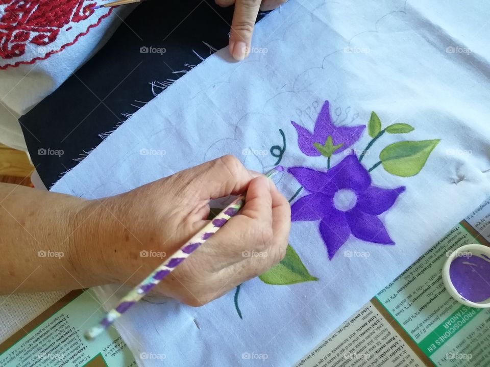 An old woman painting on fabric with acrylic paints.