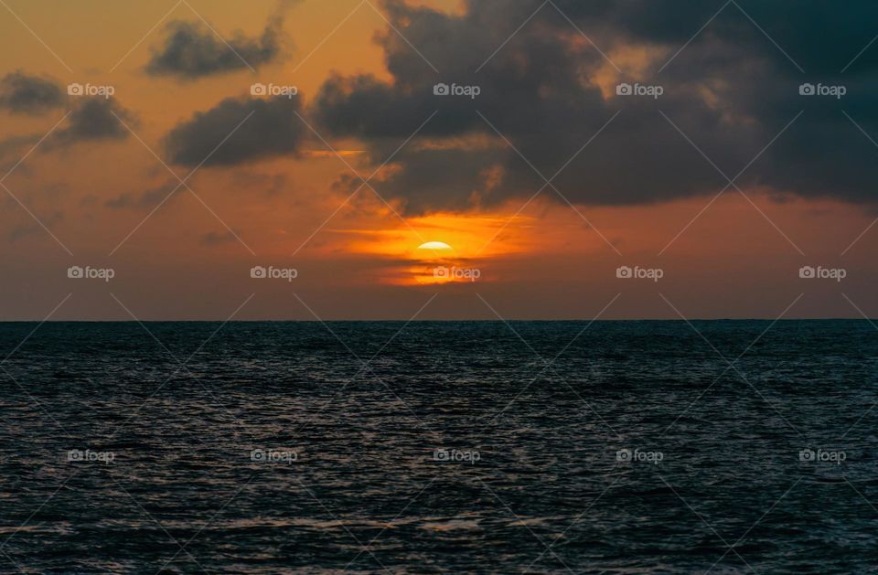 Idyllic sunset behind clouds above horizon over the ocean