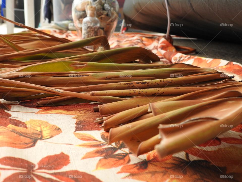 Autumn fall decor and cloth with orange drawings of leaves, vase and seashells in a bottle and dry palm leaves branches on a step during camping by a tent.