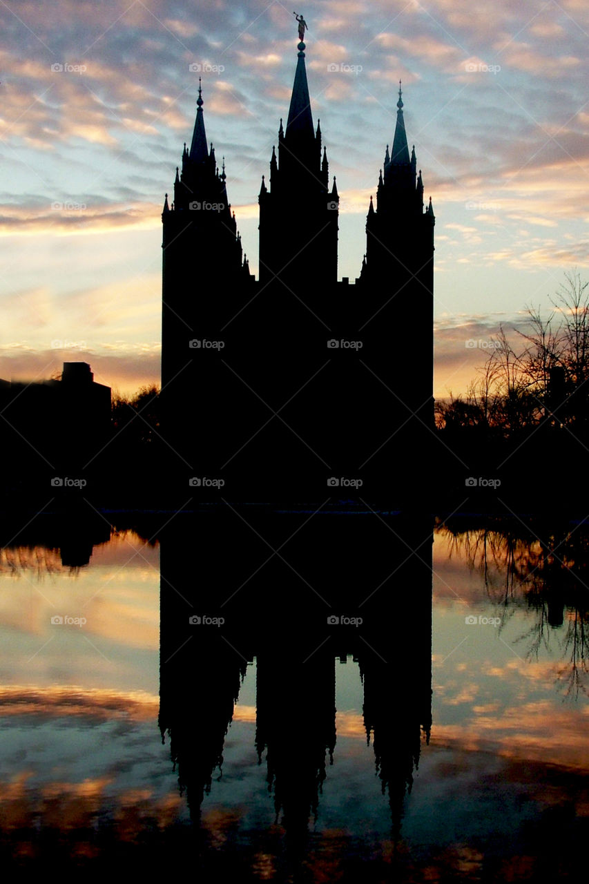 Salt Lake City LDS temple silhouetted in the evening sunset and reflected on the reflection pond with purple skies.