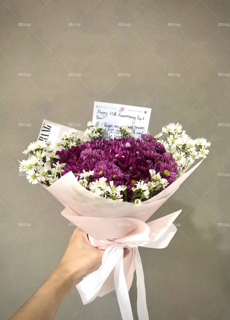 A bouquet of aster flowers wrapped in a pink paper and white ribbon
