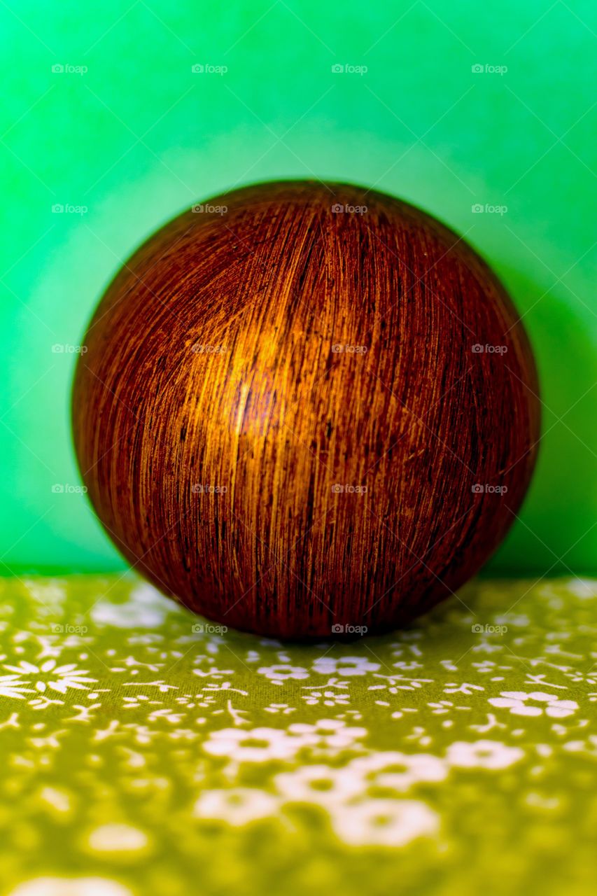 Bronze orb with dark lines against a pastel green backdrop with green and flowers beneath
