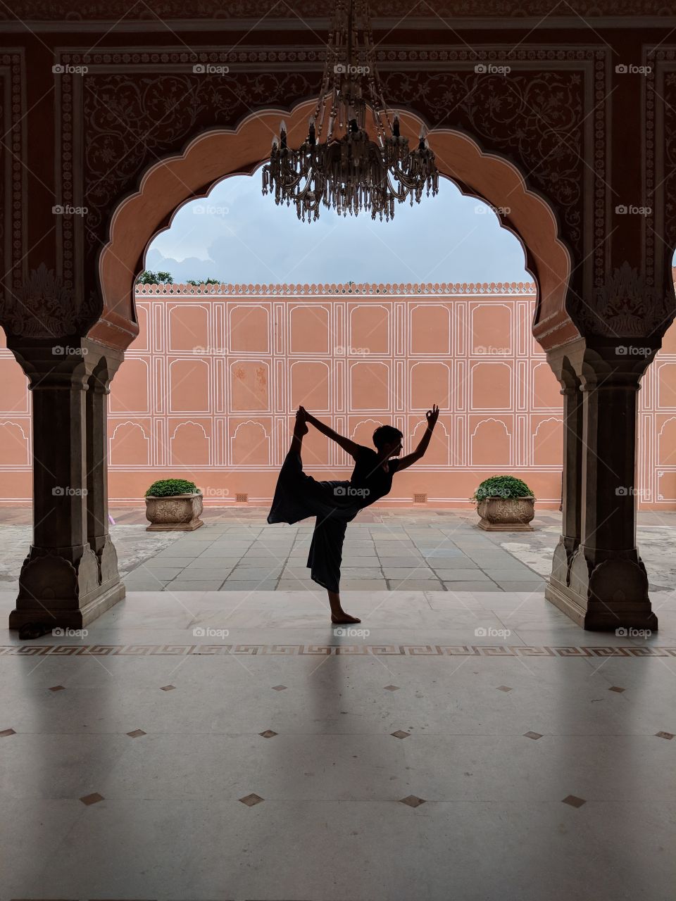 Backlit silhouette of a woman standing in a yoga pose inside a vibrant temple in Jaipur, India